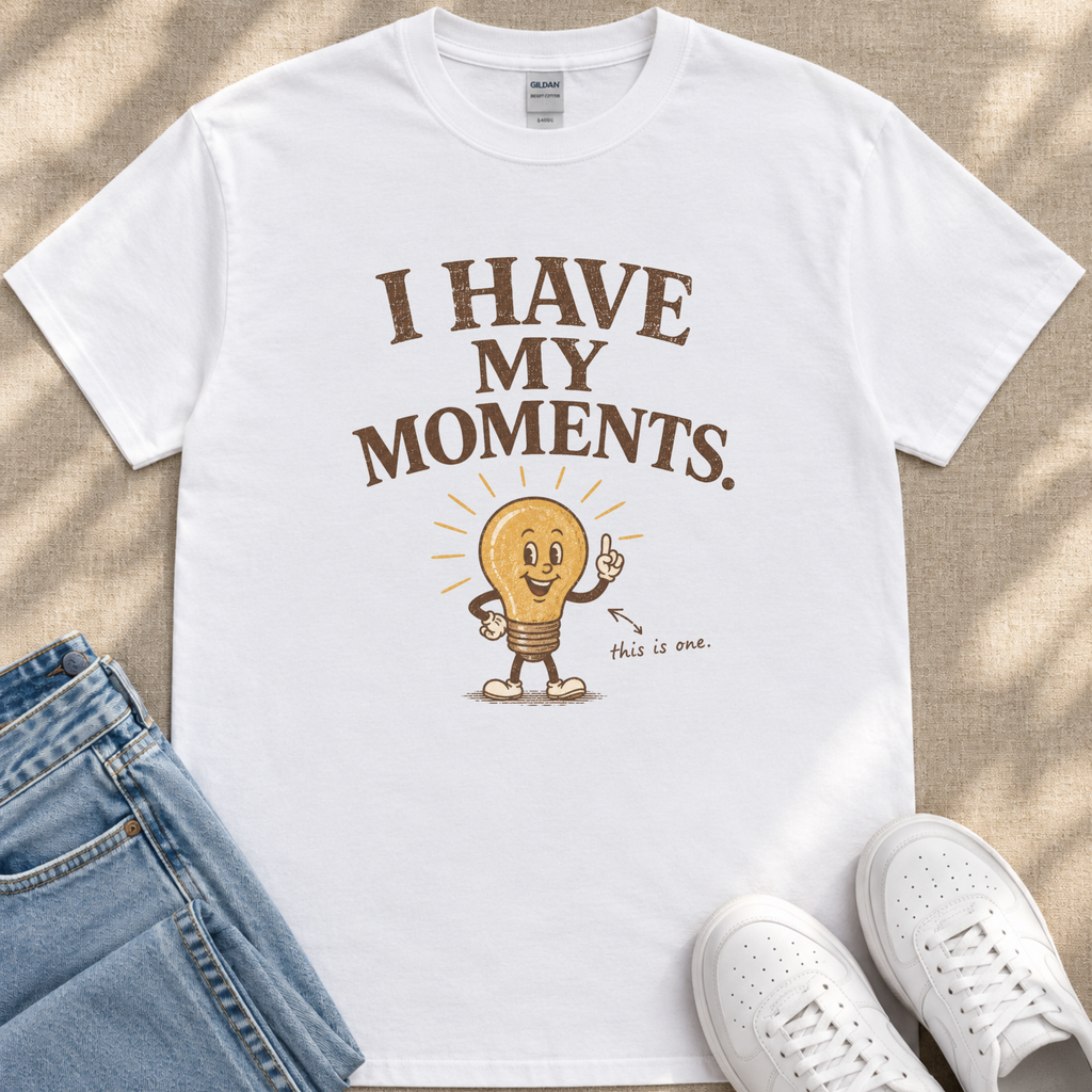 A white t-shirt with a light bulb graphic and text, along with a pair of jeans and white sneakers, laid out on a beige surface.
