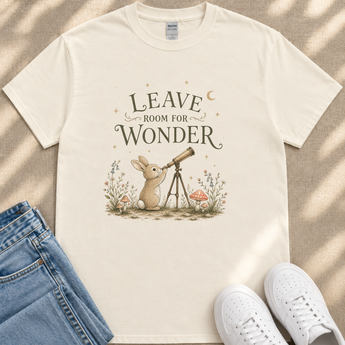 A white t-shirt with a whimsical illustration of a rabbit gazing through a telescope, accompanied by the text "LEAVE ROOM FOR WONDER".