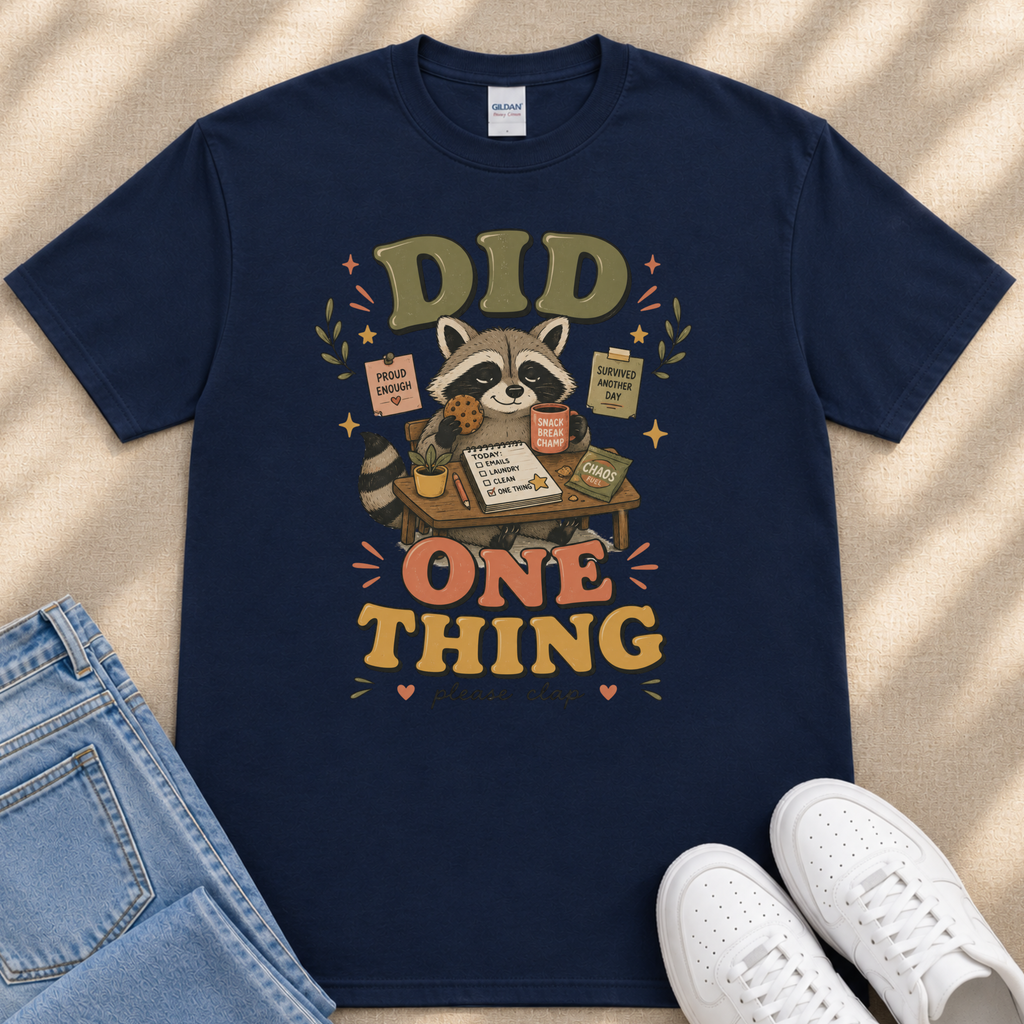 A navy blue t-shirt with a graphic design featuring a raccoon holding a sign that says "Did One Thing" and surrounded by various objects, such as a cup, a book, and a plant.