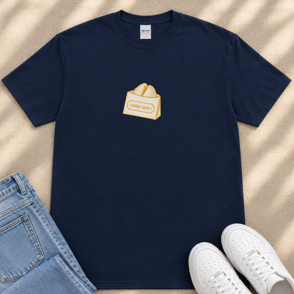 A navy blue t-shirt with a yellow graphic of a shopping bag and the text "GOOD LUCK" printed on it, along with a pair of blue jeans and white sneakers.