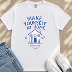 A white t-shirt with a blue graphic design and text, along with a pair of jeans and white sneakers, laid out on a beige surface.