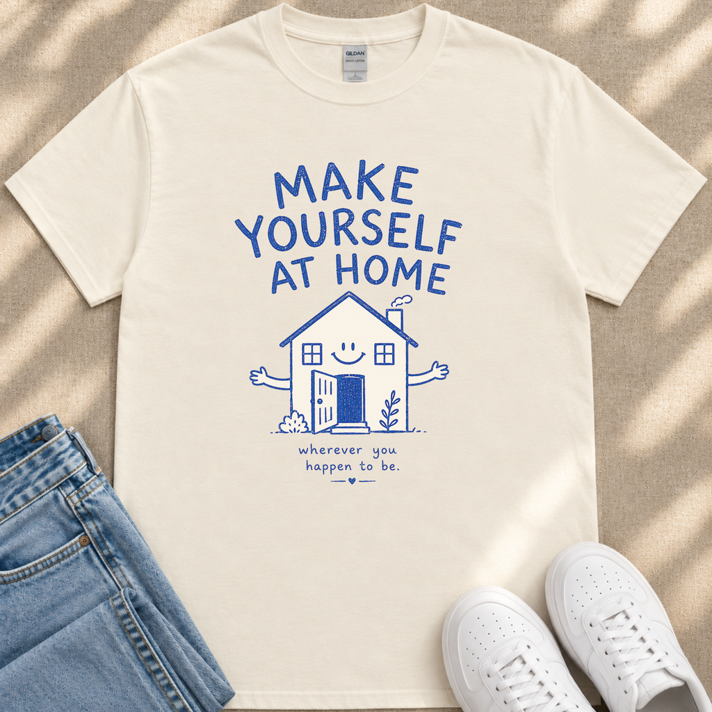 A white t-shirt with a blue graphic design and text, along with a pair of jeans and white sneakers, laid out on a beige surface.
