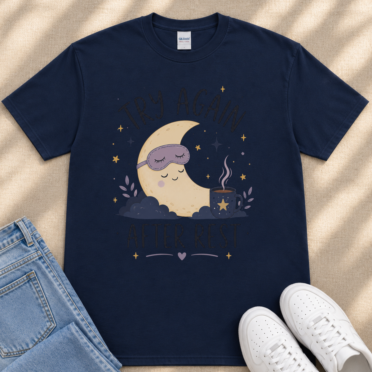 A navy blue t-shirt with a graphic design depicting a sleeping moon and stars, along with the text "TRY AGAIN AFTER REST" and a cup of tea.