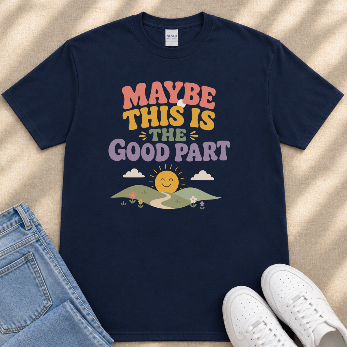 A navy blue t-shirt with a colorful graphic design and text, along with a pair of jeans and white sneakers, all laid out on a beige surface.