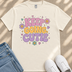 A white t-shirt with a colorful graphic design that says "KEEP GOING CUTIE" surrounded by flowers and stars. The t-shirt is placed next to a pair of jeans and white sneakers.