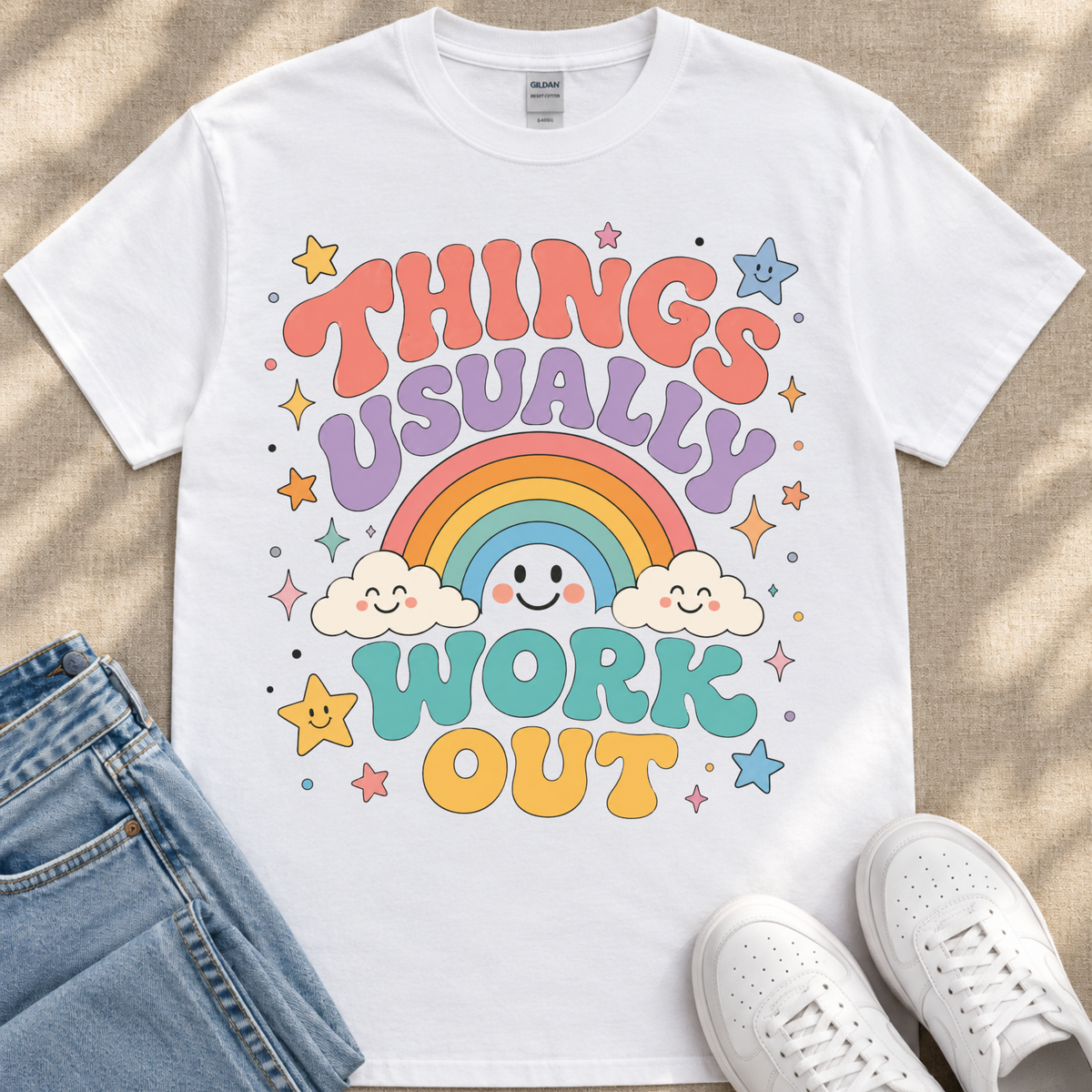 A white t-shirt with a colorful graphic design featuring a rainbow, clouds, stars, and the text "THINGS USUALLY WORK OUT"
