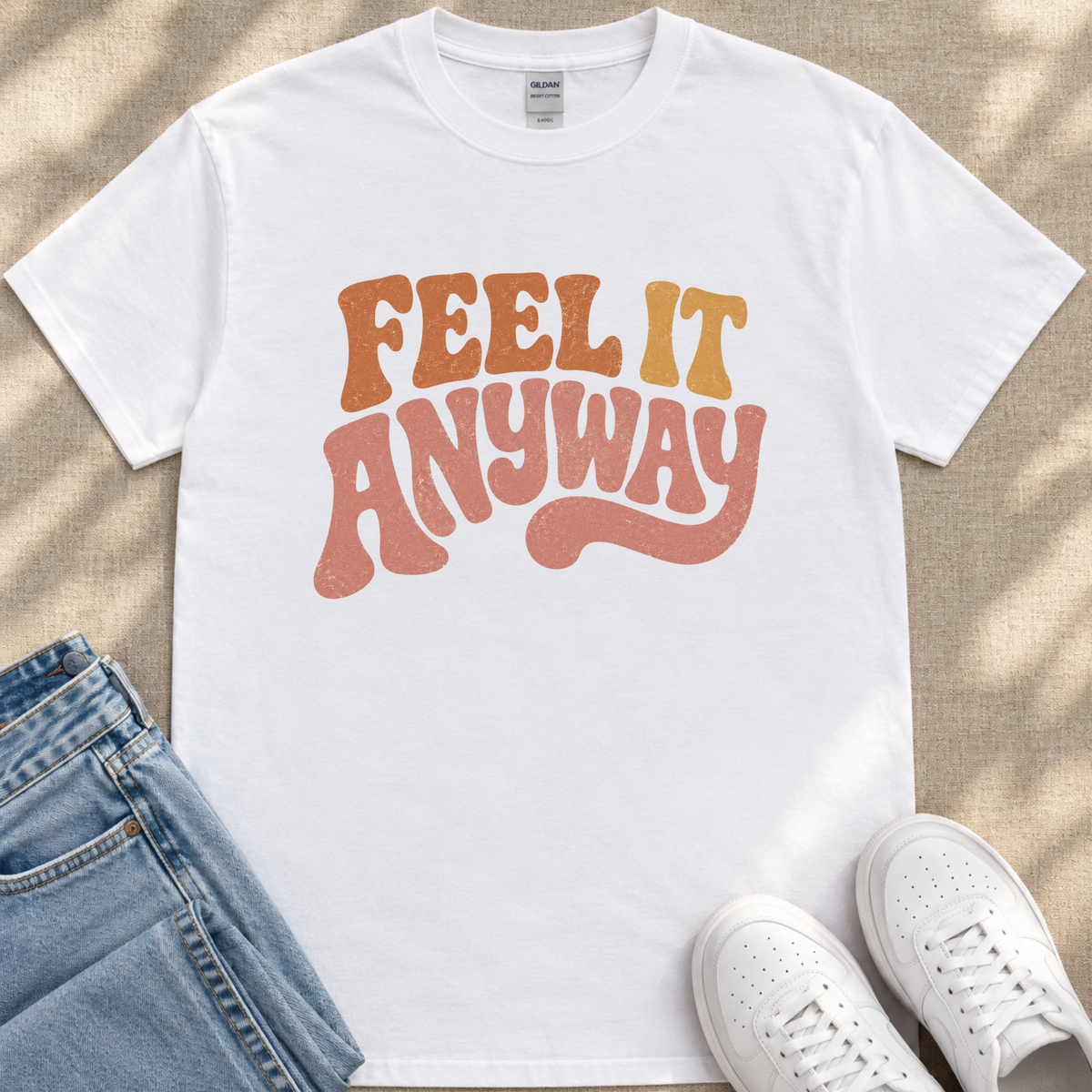 A white t-shirt with the text "FEEL IT ANYWAY" printed on it, along with a pair of blue jeans and white sneakers.