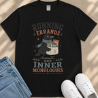 A black t-shirt with a graphic design featuring a black crow holding various items, including chips, cookies, and a bag, along with the text "RUNNING errands AND INNER MONOLOGUES".