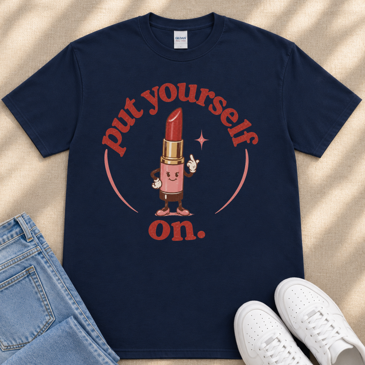 A navy blue t-shirt with a graphic design featuring a red lipstick character and the text "put yourself on."