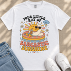 A white t-shirt with a colorful graphic design depicting a duck wearing sunglasses and holding a drink, surrounded by sun-like elements and text that reads "Your little ray of sarcastic sunshine".