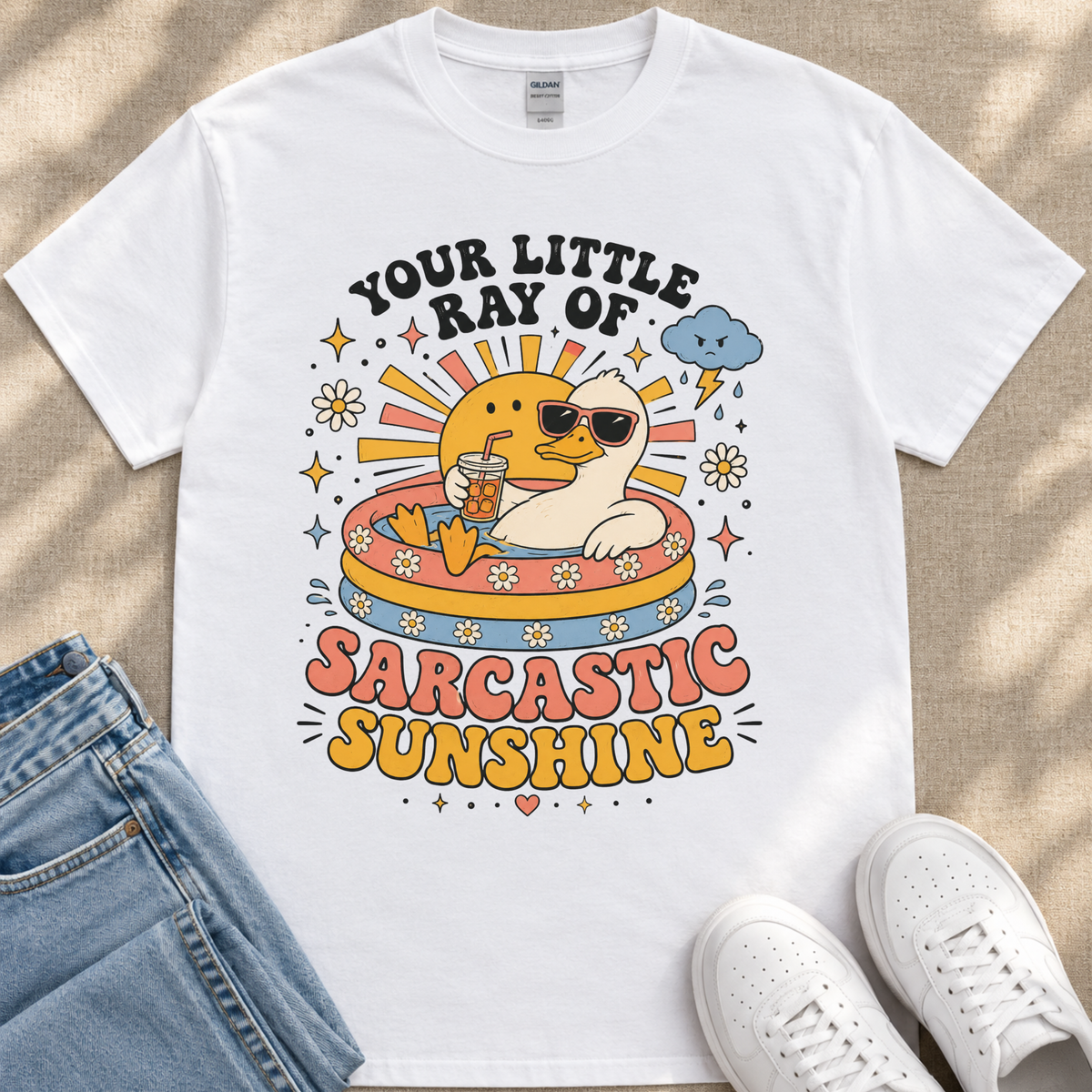 A white t-shirt with a colorful graphic design depicting a duck wearing sunglasses and holding a drink, surrounded by sun-like elements and text that reads "Your little ray of sarcastic sunshine".