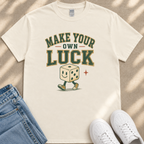 A white t-shirt with a graphic design featuring a smiling dice character and the text "MAKE YOUR OWN LUCK" printed on it.