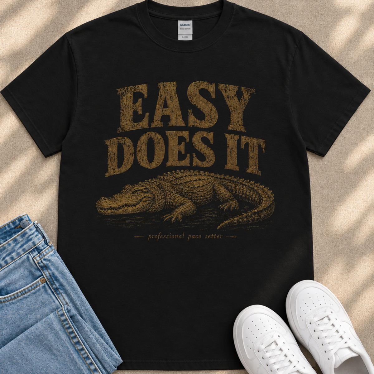 A black t-shirt with a graphic design of a crocodile and the text "EASY DOES IT" printed on it, along with the phrase "professional pace setter" below the image.