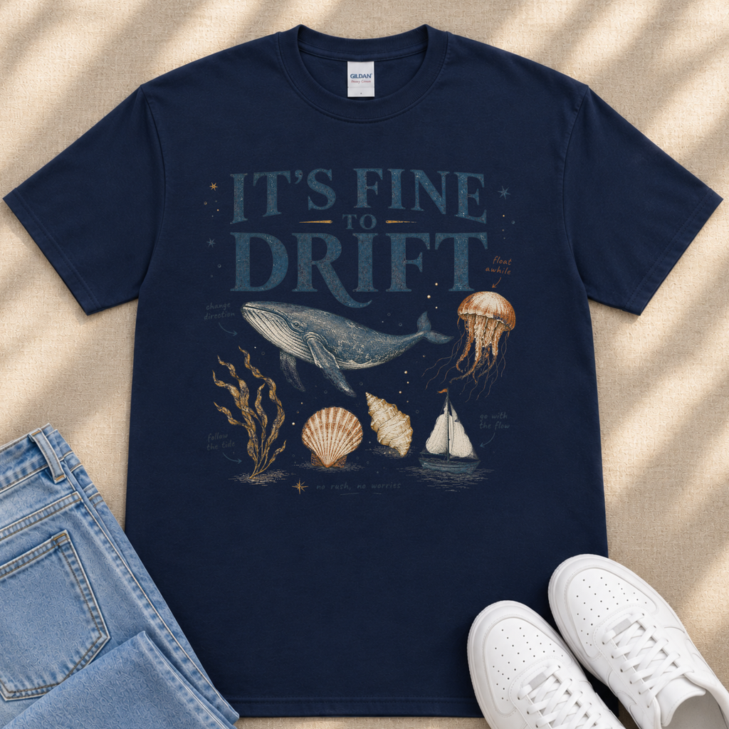 A navy blue t-shirt with a graphic design depicting a whale, jellyfish, and other marine life, along with the text "It's fine to drift". The t-shirt is placed on a beige surface, and there are a pair of jeans and white sneakers visible in the image.