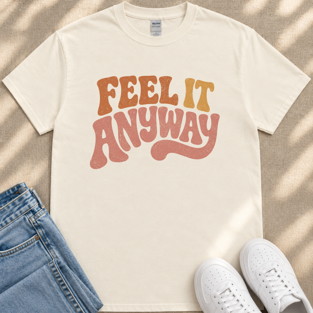 A white t-shirt with the text "FEEL IT ANYWAY" printed on it, along with a pair of blue jeans and white sneakers.