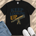 A black t-shirt with a graphic design featuring a telescope and the text "KEEP LOOKING UP" printed on it.