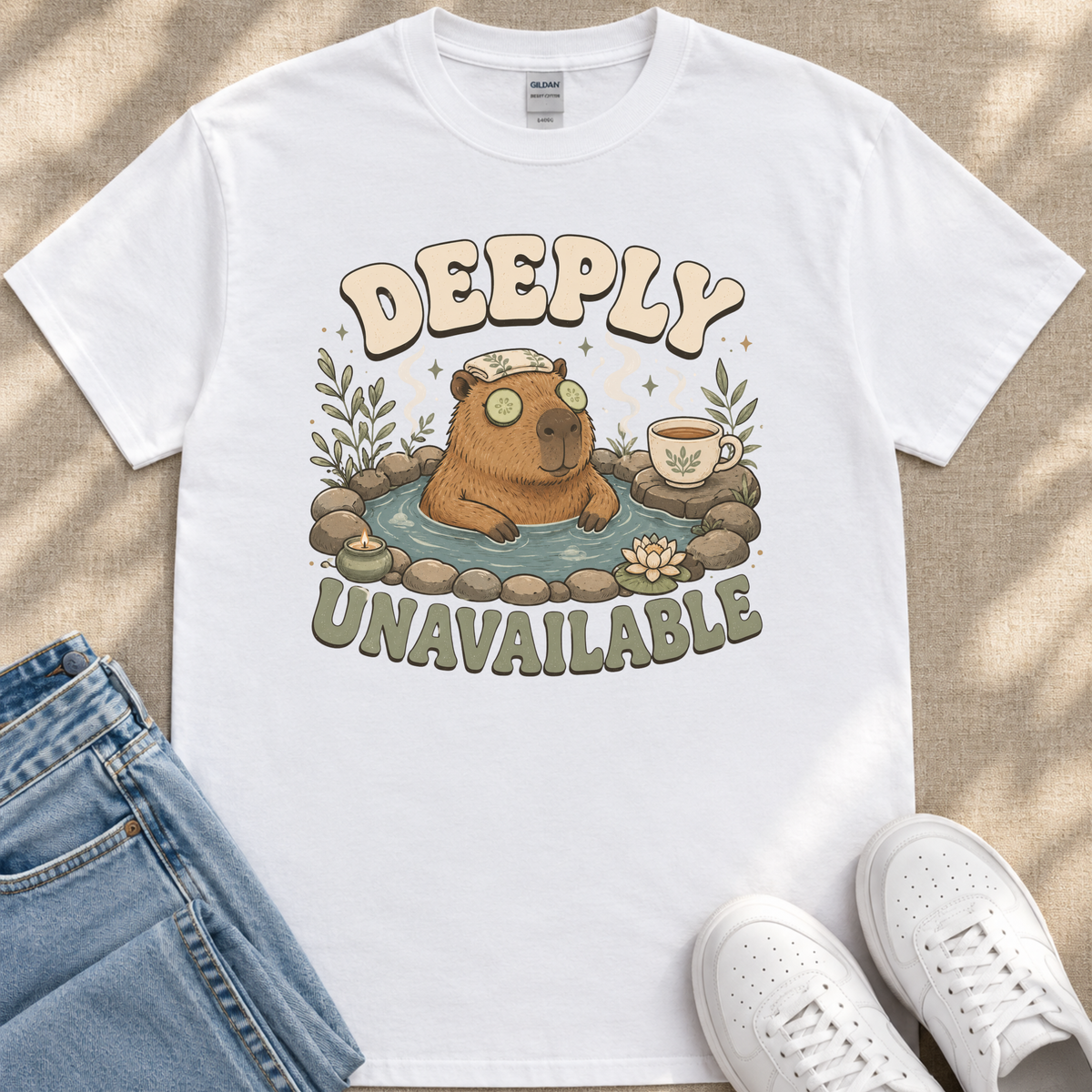 a white t-shirt with a graphic design depicting a brown bear sitting in a hot tub, surrounded by various elements such as a cup, a plant, and a pair of jeans. The text on the t-shirt reads "DEEPLY UNAVAILABLE".
