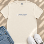 A beige t-shirt with the text "gentle reminder. you're doing okay" printed on it, along with a small envelope icon. The t-shirt is placed next to a pair of blue jeans and white sneakers, creating a casual outfit.