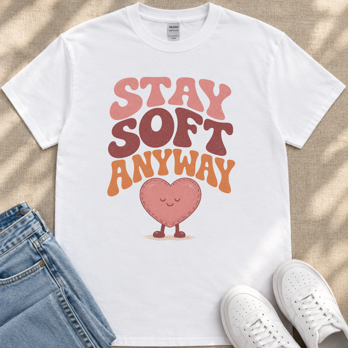 A white t-shirt with a heart-shaped graphic and the text "STAY SOFT ANYWAY" printed on it, along with a pair of jeans and white sneakers.