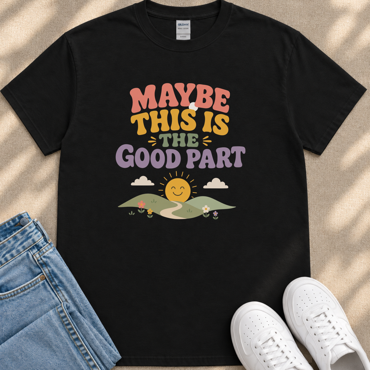 A black t-shirt with a colorful graphic design and text, along with a pair of jeans and white sneakers, laid out on a surface.