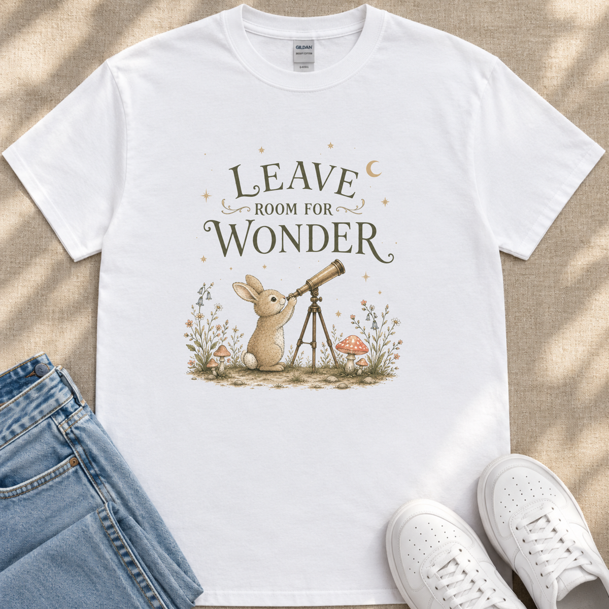 A white t-shirt with a whimsical illustration of a rabbit gazing up at the night sky, accompanied by the text "LEAVE ROOM FOR WONDER" and a crescent moon.