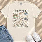 A white t-shirt with a graphic design featuring cartoon ducks and text that says "It's OKAY TO".