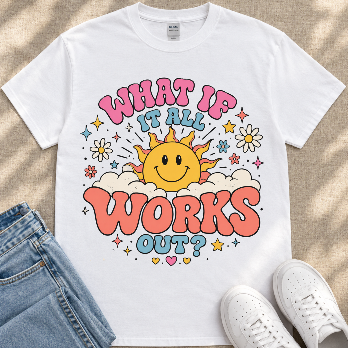 A white t-shirt with a colorful graphic design featuring a smiling sun and the text "What if it all works out?"