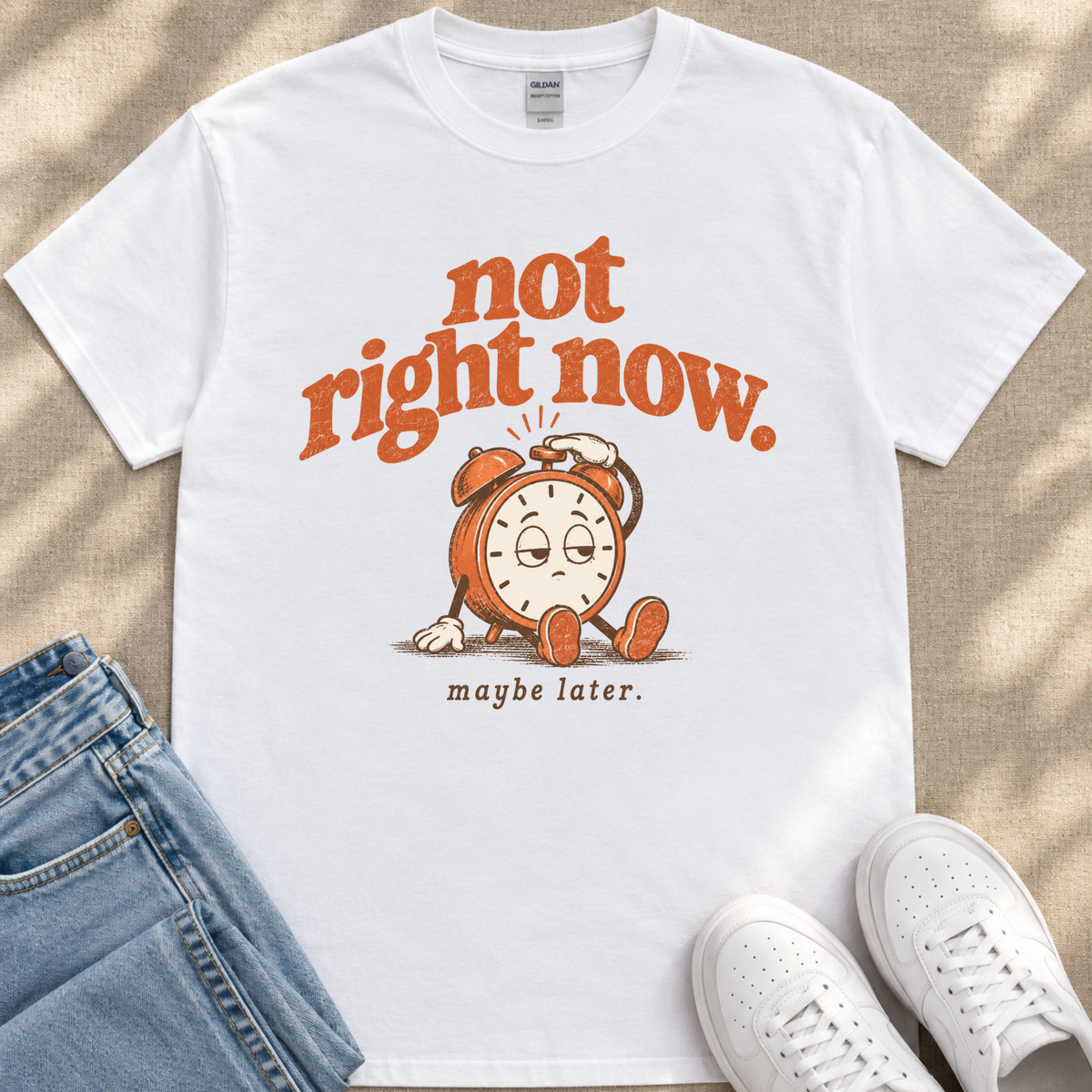 A white t-shirt with a graphic design featuring a cartoon alarm clock and the text "not right now. maybe later."