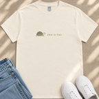 A white t-shirt with a graphic of a turtle and the text "slow is fine" printed on it, along with a pair of blue jeans and white sneakers.