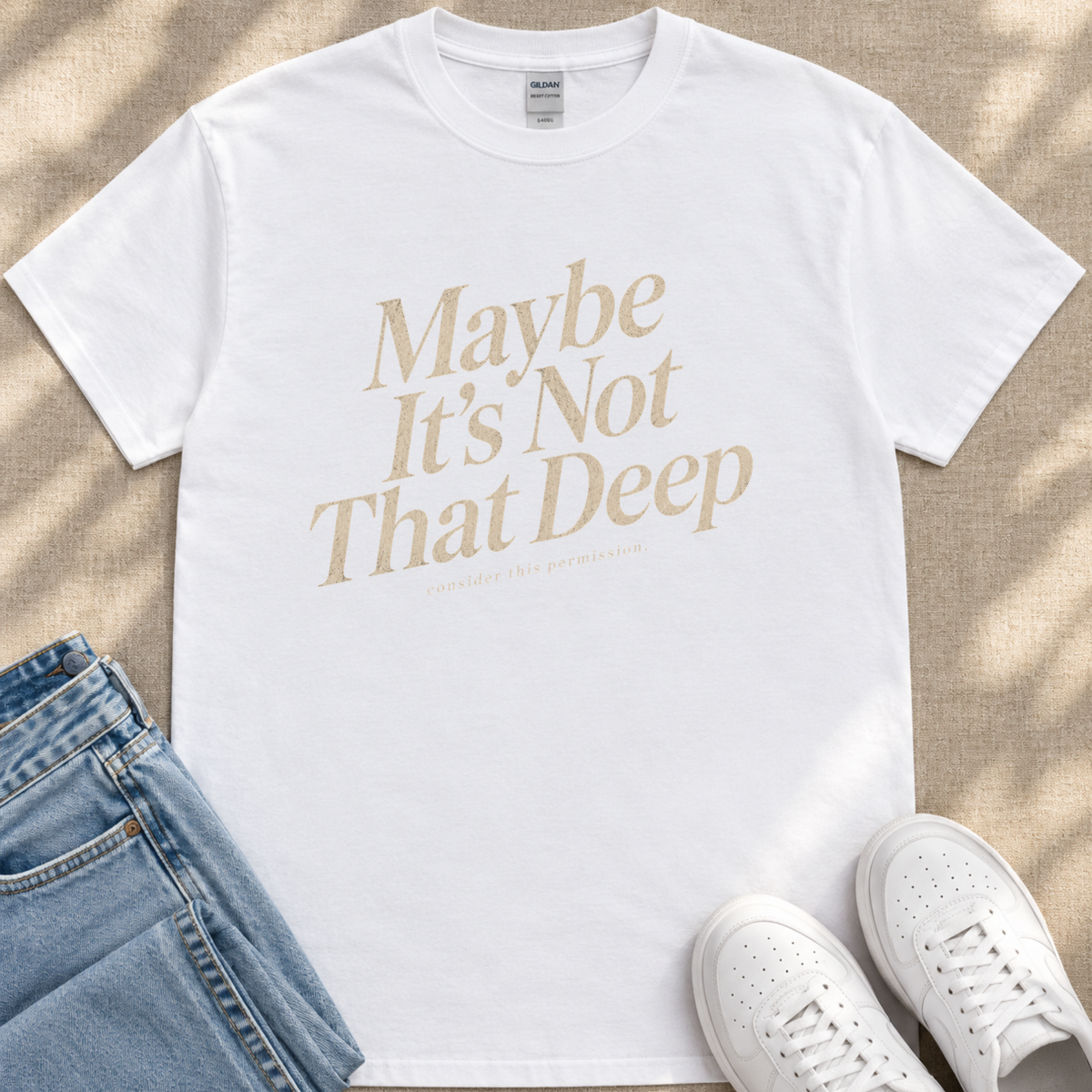 A white t-shirt with the text "Maybe It's Not That Deep" printed on it, along with a pair of blue jeans and white sneakers.