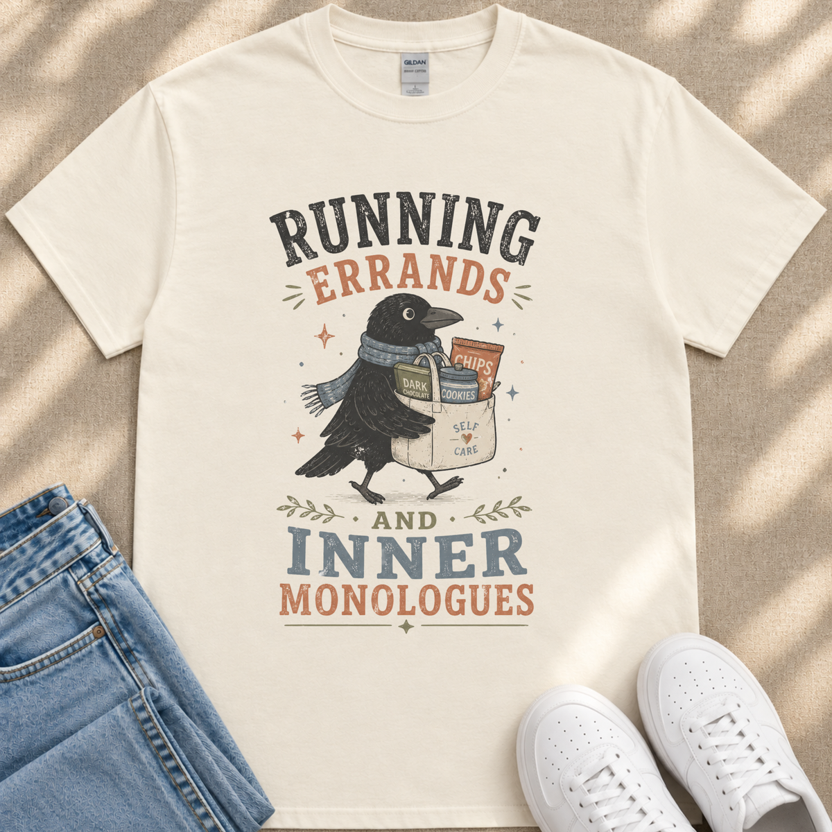 A white t-shirt with a graphic design featuring a black bird carrying a bag of chips and the text "RUNNING errands AND INNER MONOLOGUES".