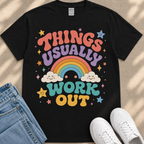 A black t-shirt with a colorful graphic design that says "THINGS USUALLY WORK OUT" along with a rainbow, clouds, stars, and a smiley face.