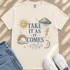 A white t-shirt with a graphic design featuring a sun, clouds, rain, and lightning, along with the text "TAKE IT AS IT COMES" and other weather-related elements.