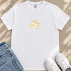 A white t-shirt with a graphic of a bag of bread, a pair of blue jeans, and white sneakers on a beige surface.