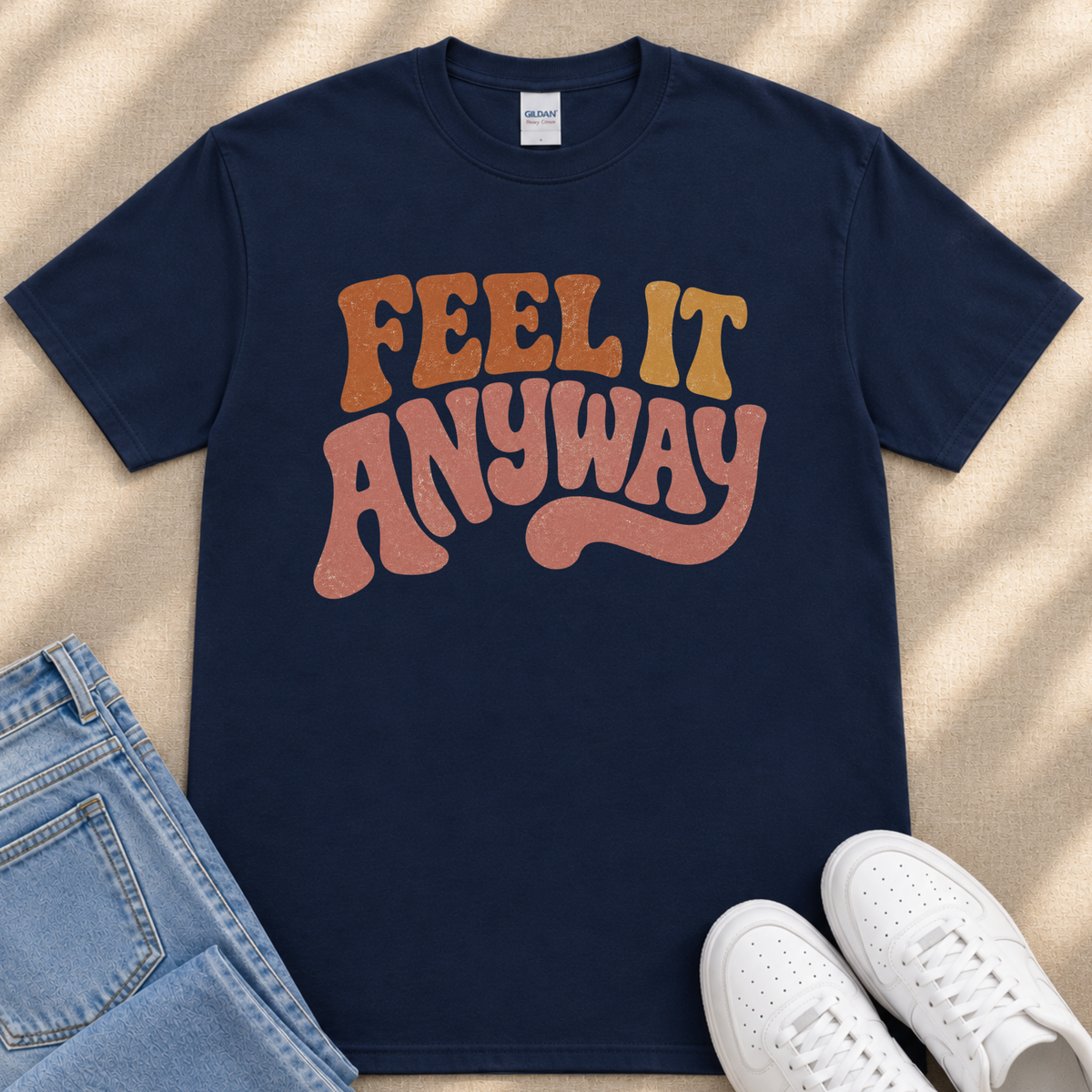 A navy blue t-shirt with the text "FEEL IT ANYWAY" printed on it, along with a pair of blue jeans and white sneakers.