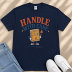 A navy blue t-shirt with a graphic design featuring a cartoon matchbox character holding a lighter and the text "HANDLE WITH CARE" printed on it.