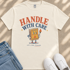 A white t-shirt with a graphic design featuring a cartoon matchbox character holding a lighter and the text "HANDLE WITH CARE" and "SAFETY MATCHES" printed on it.