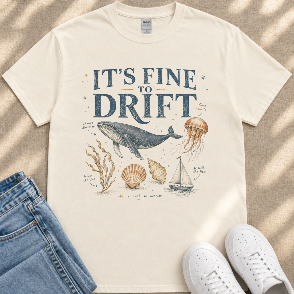 A white t-shirt with a graphic design depicting a whale, jellyfish, and other marine life, along with text that says "It's fine to drift". The t-shirt is laid out on a beige surface, and there are a pair of jeans and white sneakers visible in the image.