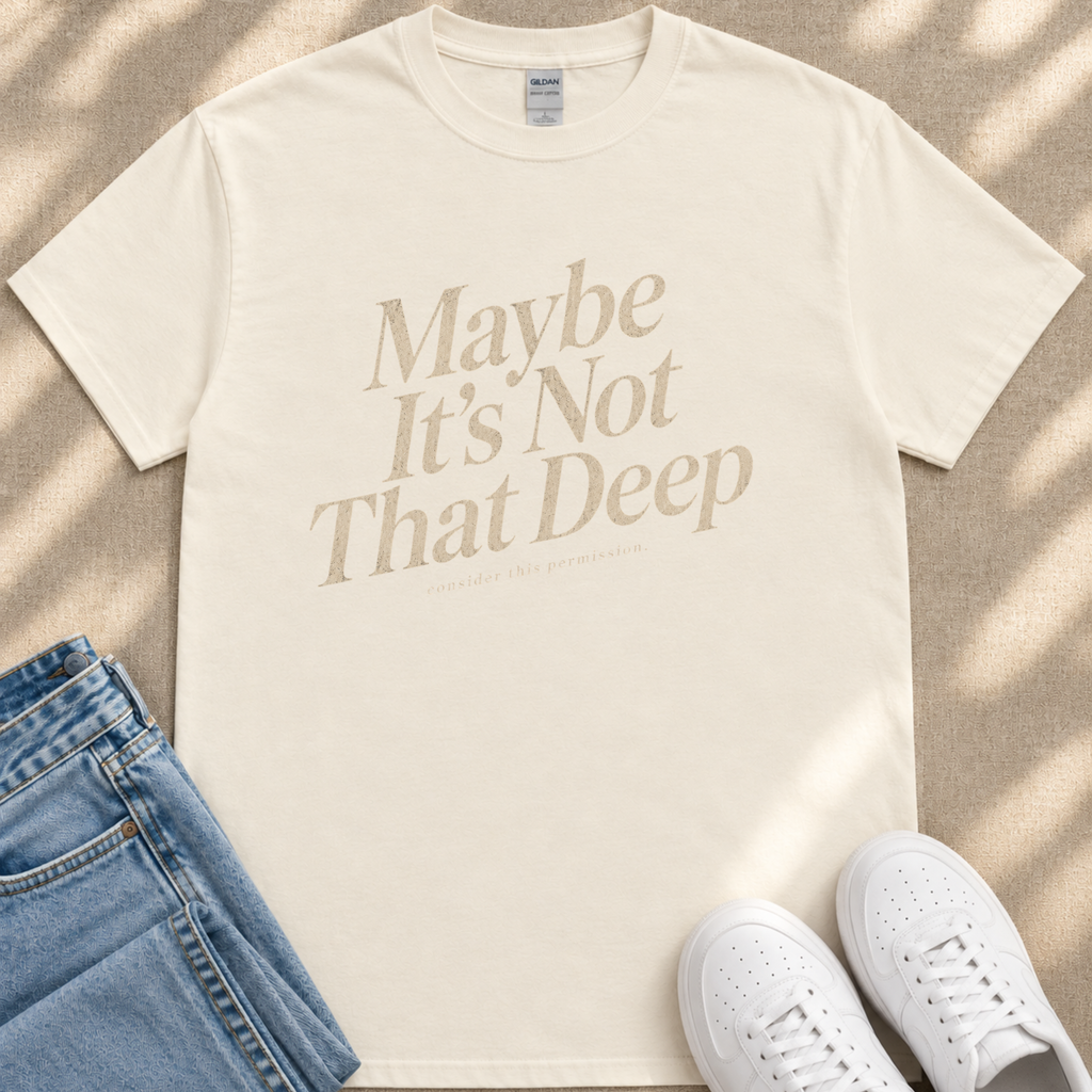 A beige t-shirt with the text "Maybe It's Not That Deep" printed on it, along with a pair of blue jeans and white sneakers.