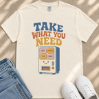 A white t-shirt with a graphic design featuring a vending machine with the text "TAKE WHAT YOU NEED" and a list of items below it.