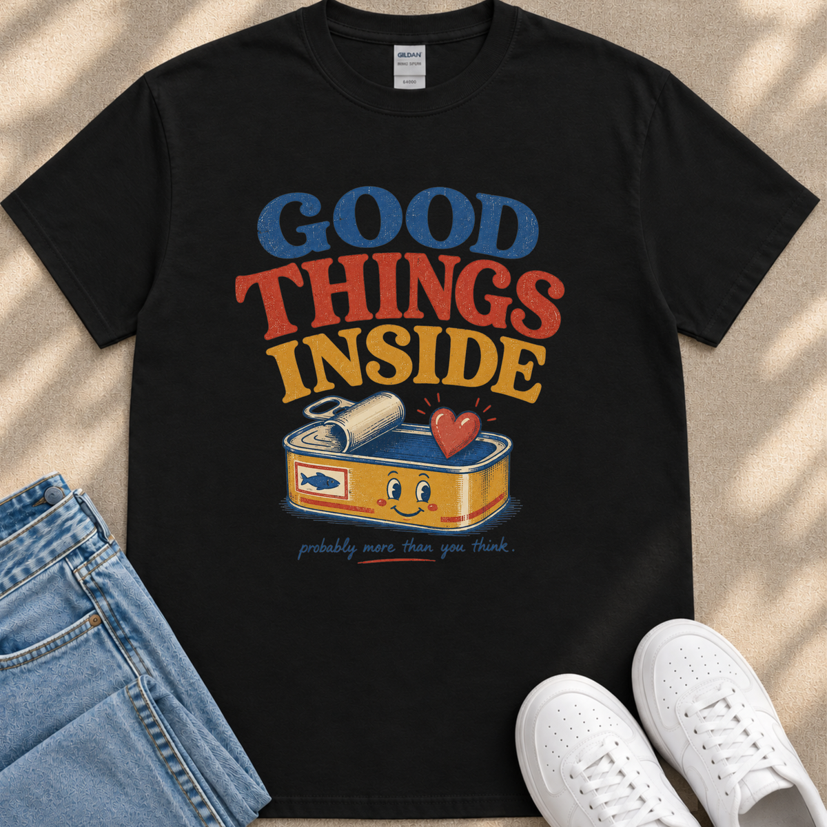 A black t-shirt with a colorful graphic design that says "GOOD THINGS INSIDE probably more than you think" and features a can of tuna with a smiling face.