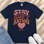 A navy blue t-shirt with a heart-shaped graphic and the text "STAY SOFT ANYWAY" printed on it, along with a pair of jeans and white sneakers.