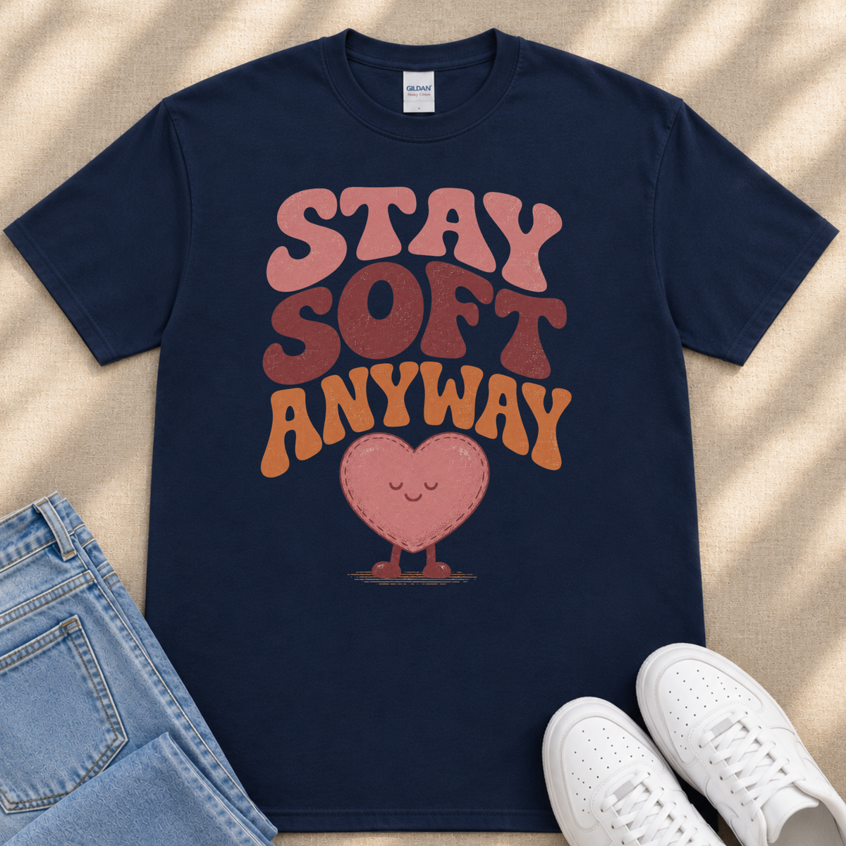 A navy blue t-shirt with a heart-shaped graphic and the text "STAY SOFT ANYWAY" printed on it, along with a pair of jeans and white sneakers.
