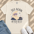 A white t-shirt with a graphic design depicting a sleeping crescent moon and stars, along with the text "TRY AGAIN AFTER REST" and a mug with a star.