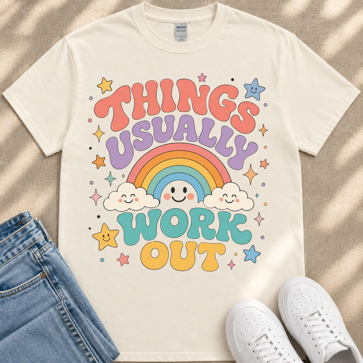 A white t-shirt with a colorful graphic design featuring a rainbow, clouds, stars, and the text "THINGS USUALLY WORK OUT"