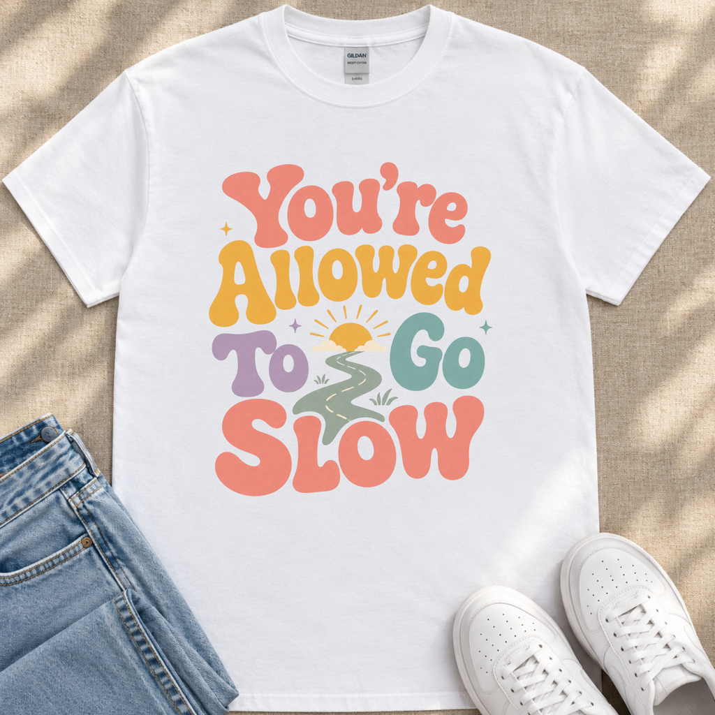 A white t-shirt with a colorful graphic design that says "You're Allowed to Go Slow" printed on it.