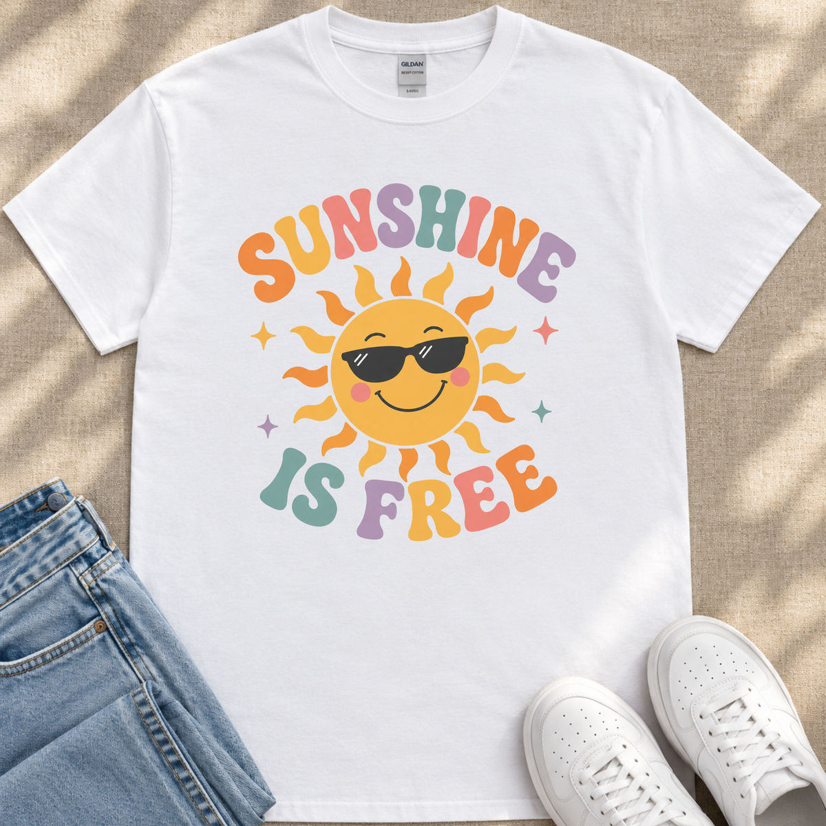 A white t-shirt with a colorful sun graphic and the text "SUNSHINE IS FREE" printed on it, along with a pair of jeans and white sneakers.