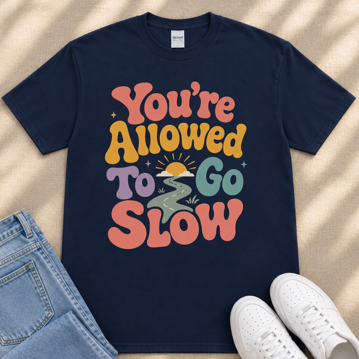A navy blue t-shirt with a colorful graphic design that says "You're Allowed to Go Slow" in a retro style.
