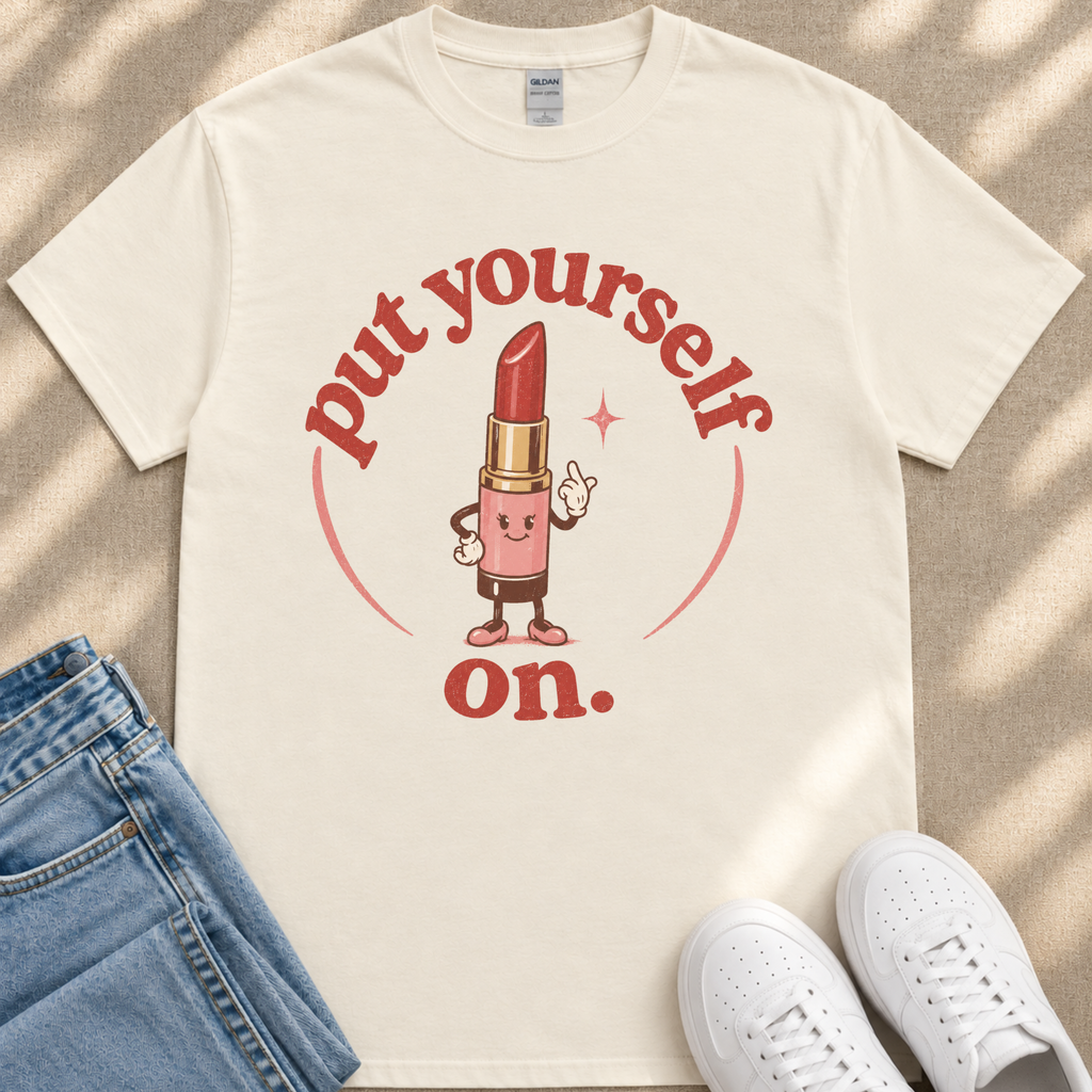 A white t-shirt with a graphic design featuring a lipstick character and the text "put yourself on."