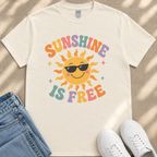 A white t-shirt with a cheerful sun graphic and the text "SUNSHINE IS FREE" printed on it, along with a pair of blue jeans and white sneakers.
